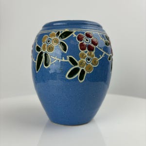 Könnte beinhalten: Eine kleine, blaue Keramikvase mit Blumenmuster. Die Vase hat einen runden Körper und eine schmale Öffnung. Die Blumen sind in Gelb-, Rot- und Grüntönen bemalt.