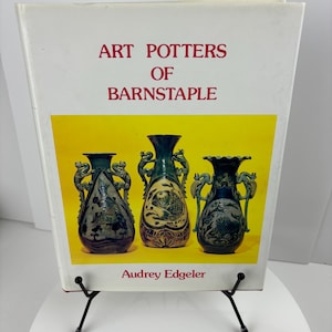 May include: A book titled "Art Potters of Barnstaple" by Audrey Edgelar. The cover features a yellow background with three blue and green ceramic vases with dragon and fish designs.