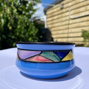 Peut inclure: Un petit bol en céramique bleu avec un motif géométrique coloré autour du bord. Le bol est sur une surface blanche.