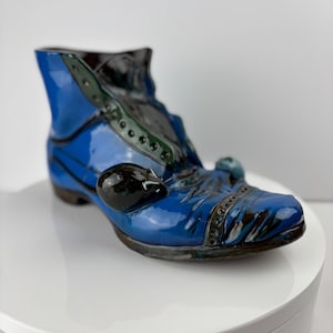 May include: A blue ceramic boot with black and green accents. The boot has a glossy finish and is decorated with a black ceramic buckle.