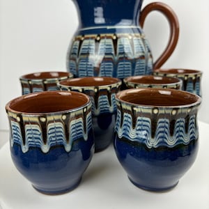 May include: A set of six blue and brown ceramic mugs with a traditional folk art design, and a matching pitcher.