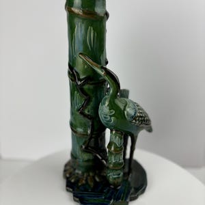 Könnte beinhalten: Eine grüne Keramikvase in Form eines Bambusstocks mit einem grünen Vogel darauf. Die Vase hat ein detailliertes Design aus Blättern und Ranken.