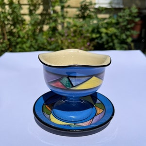Peut inclure: Une tasse en céramique bleue avec un motif géométrique coloré repose sur une soucoupe assortie. La tasse a un bord large et une base arrondie.