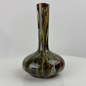 Puede incluir: Un jarrón decorativo de cerámica con base bulbosa y cuello alto y delgado. El jarrón presenta un acabado brillante con una mezcla de colores marrón, verde y blanco, creando un efecto marmoleado. El jarrón mide aproximadamente 25 cm de altura.