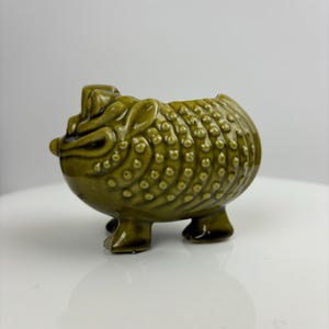 May include: A green ceramic frog planter with a textured surface and four legs. The frog planter is a unique and decorative piece for any home.