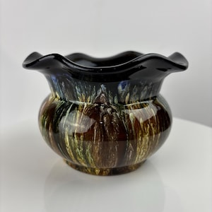 Puede incluir: Un pequeño macetero de cerámica negra con un borde ondulado y un esmalte marmoleado marrón, verde y azul.