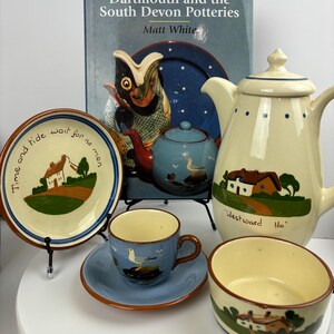 Könnte beinhalten: Eine Sammlung von Keramik mit einer blau-weißen Teetasse und Untertasse, einer cremefarbenen Teekanne, einer cremefarbenen Schüssel mit grünem und braunem Design und einem blau-weißen Teller mit dem Text "Time and tide wait for no man".