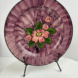 Peut inclure: Une assiette en céramique violette avec un bord noir et un motif peint à la main de fleurs roses avec des feuilles vertes.