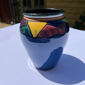 Peut inclure: Un vase en céramique bleu avec un motif géométrique dans des tons de vert, jaune, rouge et marron.