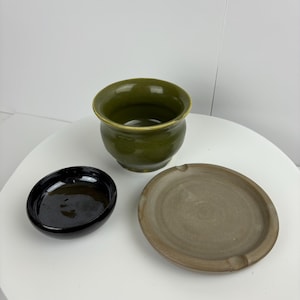 Puede incluir: Tres platos de cerámica: un cuenco verde, un cuenco negro y un platillo marrón.
