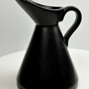 May include: A black ceramic pitcher with a wide spout and a handle. The pitcher has a conical shape and a smooth, glossy finish.