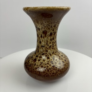Könnte beinhalten: Eine kleine, braune und weiße Keramikvase mit einem gesprenkelten Überzug. Die Vase hat einen schmalen Hals und einen runden Körper.