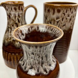 May include: Three brown ceramic vases with a white glaze. The vases have a mottled brown and white pattern. The vases are all different sizes and shapes.