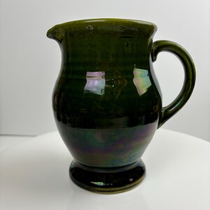 May include: A dark green ceramic jug with an iridescent glaze. The jug has a rounded body and a flared lip.