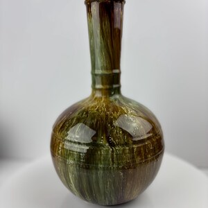 May include: A decorative vase with a round base and a long, slender neck. The vase has a glossy finish with a blend of green, brown, and gold tones. The vase is approximately 25 cm tall.