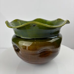 Puede incluir: Una maceta de cerámica verde y marrón con un borde ondulado y una superficie texturizada.