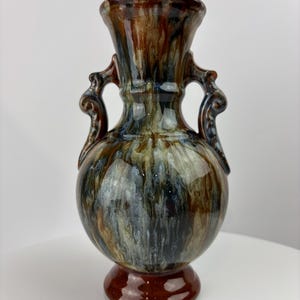 May include: A brown and blue ceramic vase with two handles. The vase has a mottled glaze with brown, blue, and white streaks.