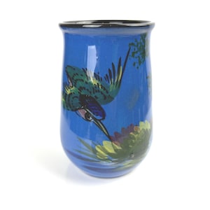 Peut inclure: Un vase en céramique bleu avec un motif de colibri peint. Le colibri est vert, bleu et jaune avec des accents noirs. Le vase a un bord noir.