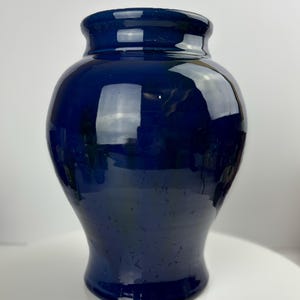 Könnte beinhalten: Eine tiefblaue Keramikvase mit rundem Korpus und leicht ausgestellter Öffnung. Die Vase hat eine glänzende Oberfläche und einen dezenten Glanz.