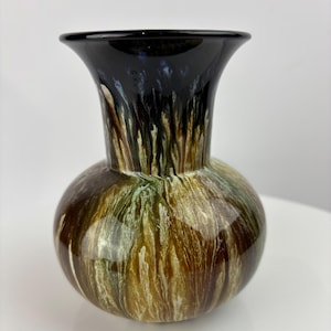 Puede incluir: Un pequeño jarrón redondo de cerámica con un borde negro y un patrón de remolino de esmalte marrón, verde y blanco.