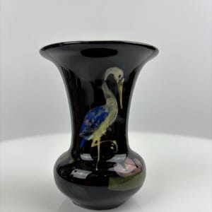 Può includere: Un vaso in ceramica nera con bordo svasato e base bulbosa. Il vaso presenta un disegno dipinto a mano di un airone con accenti blu, gialli e bianchi. Il vaso ha una finitura lucida, che mette in risalto l'opera d'arte dettagliata.