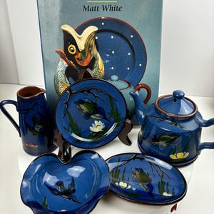 Könnte beinhalten: Ein Set aus blauer und weißer Keramik mit Vogelmotiv. Das Set beinhaltet eine Teekanne, eine Milchkännchen, eine kleine Schüssel und zwei Teller. Das Buch "Dartmouth and the South Devon Potteries" von Matt White befindet sich im Hintergrund.