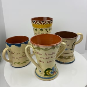 Könnte beinhalten: Vier Keramikbecher mit handbemalten Designs und Sprüchen. Die Becher sind in verschiedenen Formen und Größen, zwei davon mit Henkeln. Die Sprüche auf den Bechern lauten "An' soa my will a Yorksh", "Little boats must keep the shore" und "dows ne".