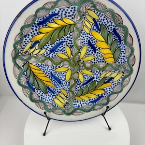 May include: A decorative ceramic plate with a blue, green, and yellow floral design. The plate is on a black metal stand.