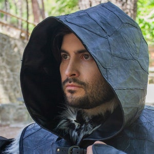 May include: A black leather hooded cloak with a fur collar and buckles. The hood is made of multiple pieces of leather sewn together.