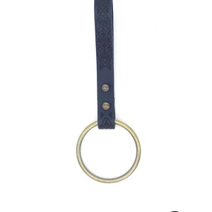 May include: A black leather sword hanger with an ornate design and a brass ring.