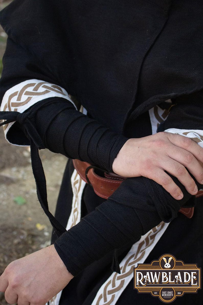 May include: Black fabric arm warmers with a braided design. The arm warmers are tied at the wrist with a black cord. The arm warmers are worn over a black robe with a white and brown braided design.