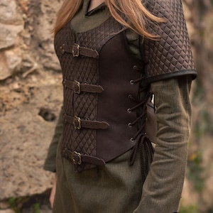 May include: Brown leather vest with a quilted design and multiple buckles. The vest has a lace-up back and a matching shoulder piece.