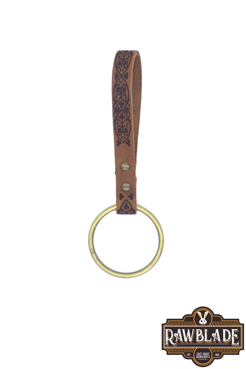 May include: A brown leather key chain with a brass ring and a decorative pattern. The key chain is made by Rawblade East Coast Merchants.