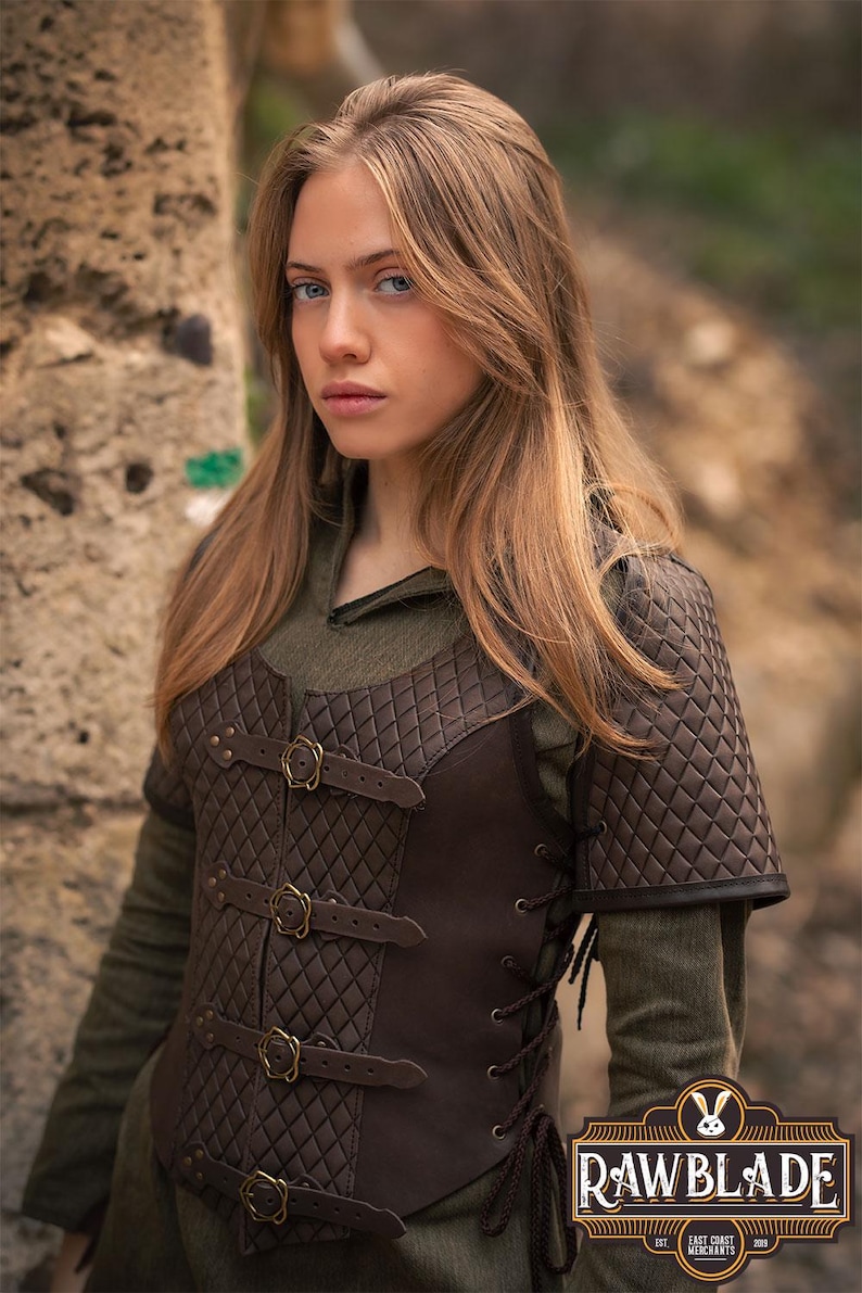 May include: A brown leather vest with a quilted pattern and multiple buckles. The vest has a lace-up back and is worn over a green shirt. The vest is labeled "Rawblade East Coast Merchants"