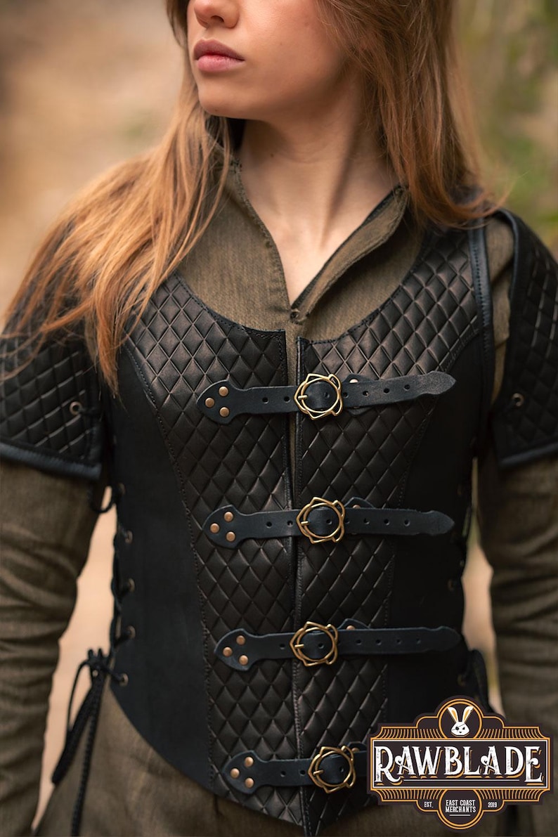 May include: Black leather vest with a quilted diamond pattern and gold buckles. The vest has a lace-up back and is worn over a green shirt. The vest is labelled "Rawblade East Coast Merchants 2018".
