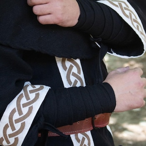May include: Black hooded robe with white and brown trim. The trim features a Celtic knot design. The robe has a brown leather belt.