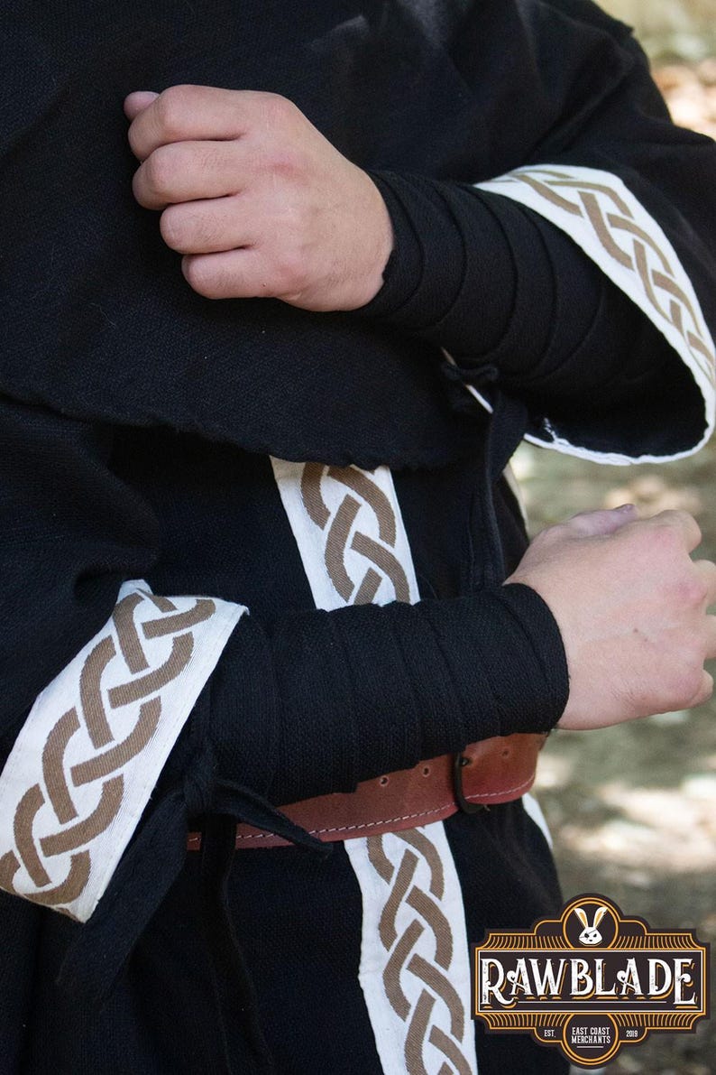 May include: Black hooded robe with white and brown trim. The trim features a Celtic knot design. The robe has a brown leather belt.