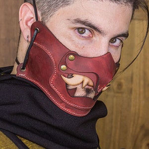 May include: A burgundy leather mask with a stylized design, featuring brass rivets and a stitched border. The mask has a cutout revealing a portion of a face. The words "BLACK LABEL" are visible. The Rawblade logo is in the bottom right corner.