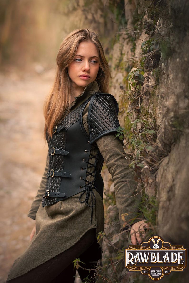 May include: A black leather vest with a quilted design and buckles. The vest has a laced-up front and shoulder pads. The vest is worn by a person standing in front of a stone wall.