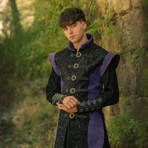 May include: A black and purple medieval-style vest with ornate detailing and gold-colored clasps. The vest features a high collar and shoulder accents. The Rawblade logo is visible in the lower right corner. The vest is worn over a black long-sleeve shirt.