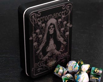 Könnte beinhalten: Eine schwarze Metallbox mit einem Design einer Kapuzenfigur mit Schädeln und dem Text "Necromancer" und "Never walk alone". Die Box steht auf einer schwarzen Oberfläche mit sieben grünen, schwarzen und weißen Würfeln.