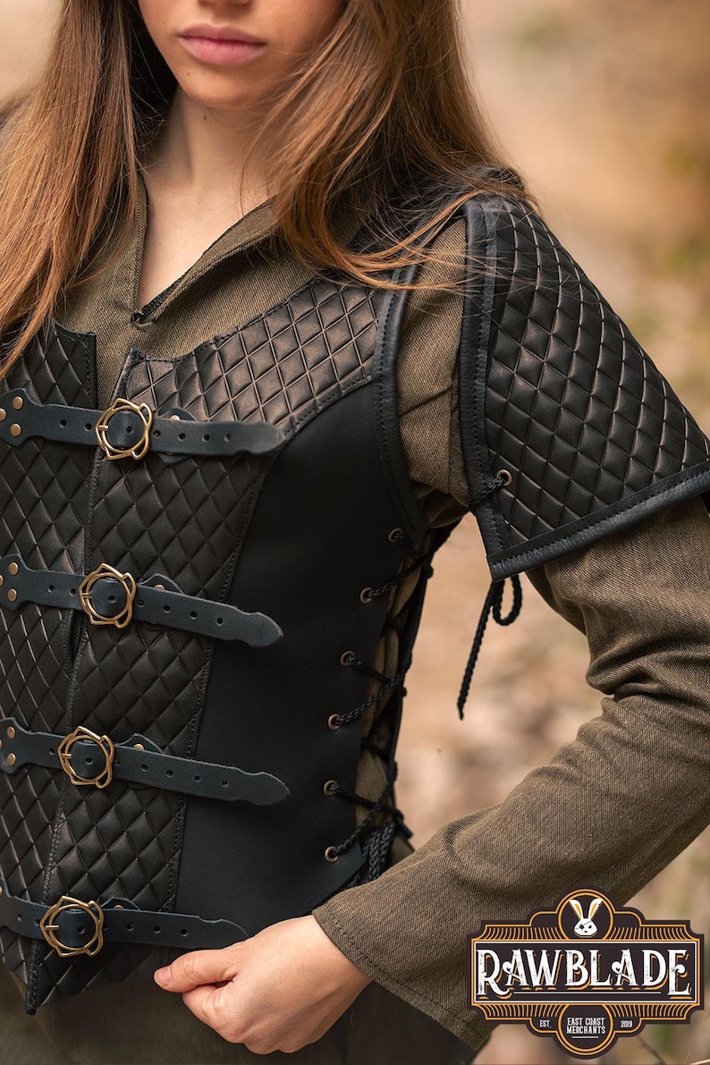 May include: Black leather armour vest with a quilted design and brass buckles. The vest has a lace-up back and is worn over a brown shirt. The vest has shoulder pads with a quilted design.