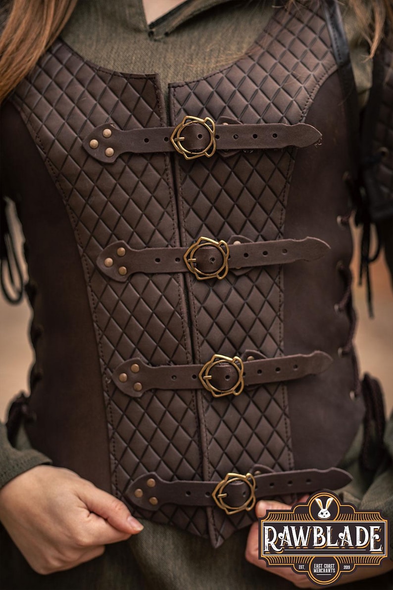May include: A brown leather vest with a quilted diamond pattern and four adjustable straps with gold buckles. The vest has a laced back and is made by Rawblade East Coast Merchants.