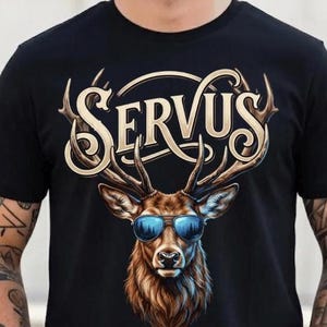 May include: Black t-shirt featuring a detailed illustration of a deer wearing blue sunglasses. The word "SERVUS" is arched above the deer's head in a decorative font. The deer has brown fur and large antlers.