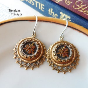 May include: A pair of gold-toned earrings with a filigree design. The earrings feature a round, dark brown cameo with a floral pattern.