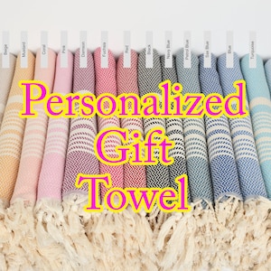 May include: A display of rolled, fringed towels in various colors, including gray, beige, pink, red, and blue. Each towel has a striped pattern and is labeled with a color name. The text "Personalized Gift Towel" is overlaid on the image.