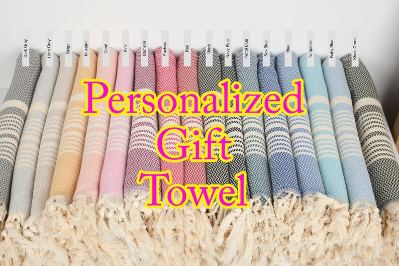 May include: A display of rolled, fringed towels in various colors, including gray, beige, pink, red, and blue. Each towel has a striped pattern and is labeled with a color name. The text "Personalized Gift Towel" is overlaid on the image.