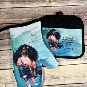 May include: A set of two oven mitts featuring a black woman with a pink shirt and blue jeans. The mitts have a turquoise background with a watercolor effect. The text "Stay Salty" is on the woman's shirt. The text "Let your speech always be with grace, seasoned with salt Colossians 4:6" is on the other mitt. The mitts are part of a collection called "Melanin Chef".