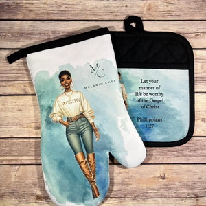 May include: A pair of oven mitts with a black and white design. One mitt features a woman with brown skin wearing a white shirt with the word "WORTHY" on it, blue jeans, and brown boots. The other mitt has a blue background with the text "Let your manner of life be worthy of the Gospel of Christ Phillippians 1:27".