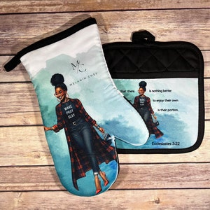May include: A set of two black and white oven mitts with a quilted design. The larger mitt features a woman with a red and black plaid shirt and the text "Wake Pray Slay". The smaller mitt features the text "that there is nothing better to enjoy their own is their portion. Ecclesiastes 3:22".